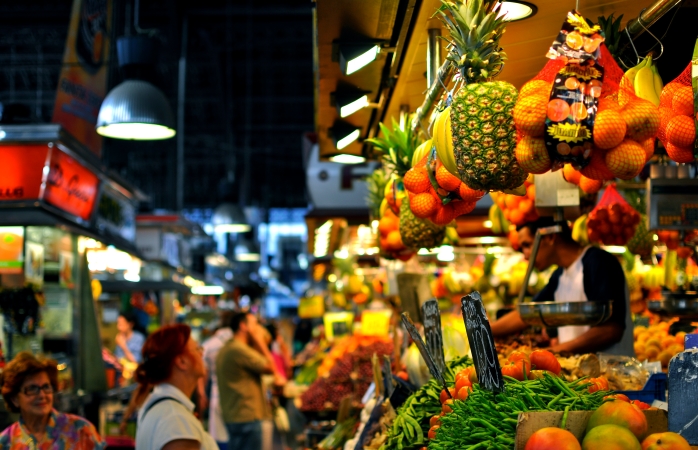 Boqueria pazarındaki meyve tezgâhının önünden geçen müşteriler.