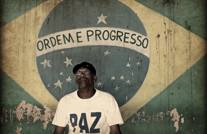 Rio favela: Brezilya'nın 'düzen ve ilerleme' sloganının altında oturan ve 'barış' yazılı bir tişört giyen adam.