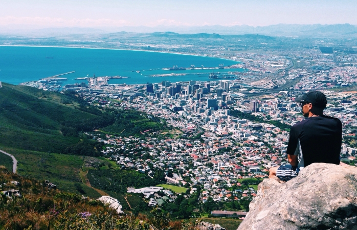 Cape Town’ın kıyı şeridine bakan bir kayanın üzerine oturan bir adam.