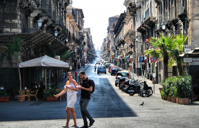 Catania'da öğle yemeklerini yerken caddeden karşıya geçen bir çift.