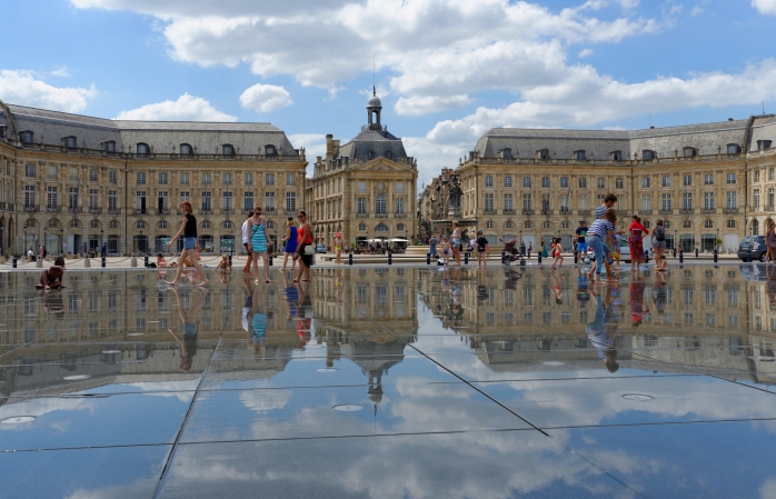 Bir grup insan Fransa, Bordeaux'daki Miroir d'eau'nun parlak su yüzeyinin keyfini çıkarıyor.
