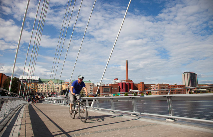 popüler tatil yerleri- Finlandiya’nın Tampere şehrindeki bir köprünün üzerinden bisikletle geçen bir adam
