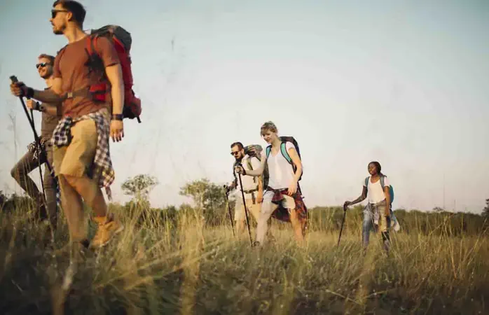 Group of young hikers, walking together through grass. Selective focus to man and woman in a middle. They enjoy sunny day. Same people you can find working in our creative office and backyard party for your coverage.