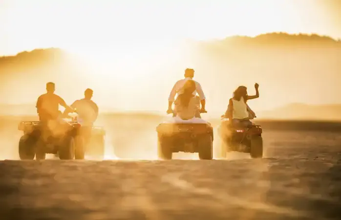 Rear view of group of people having fun while driving quad bikes in the desert at sunset. Copy space.